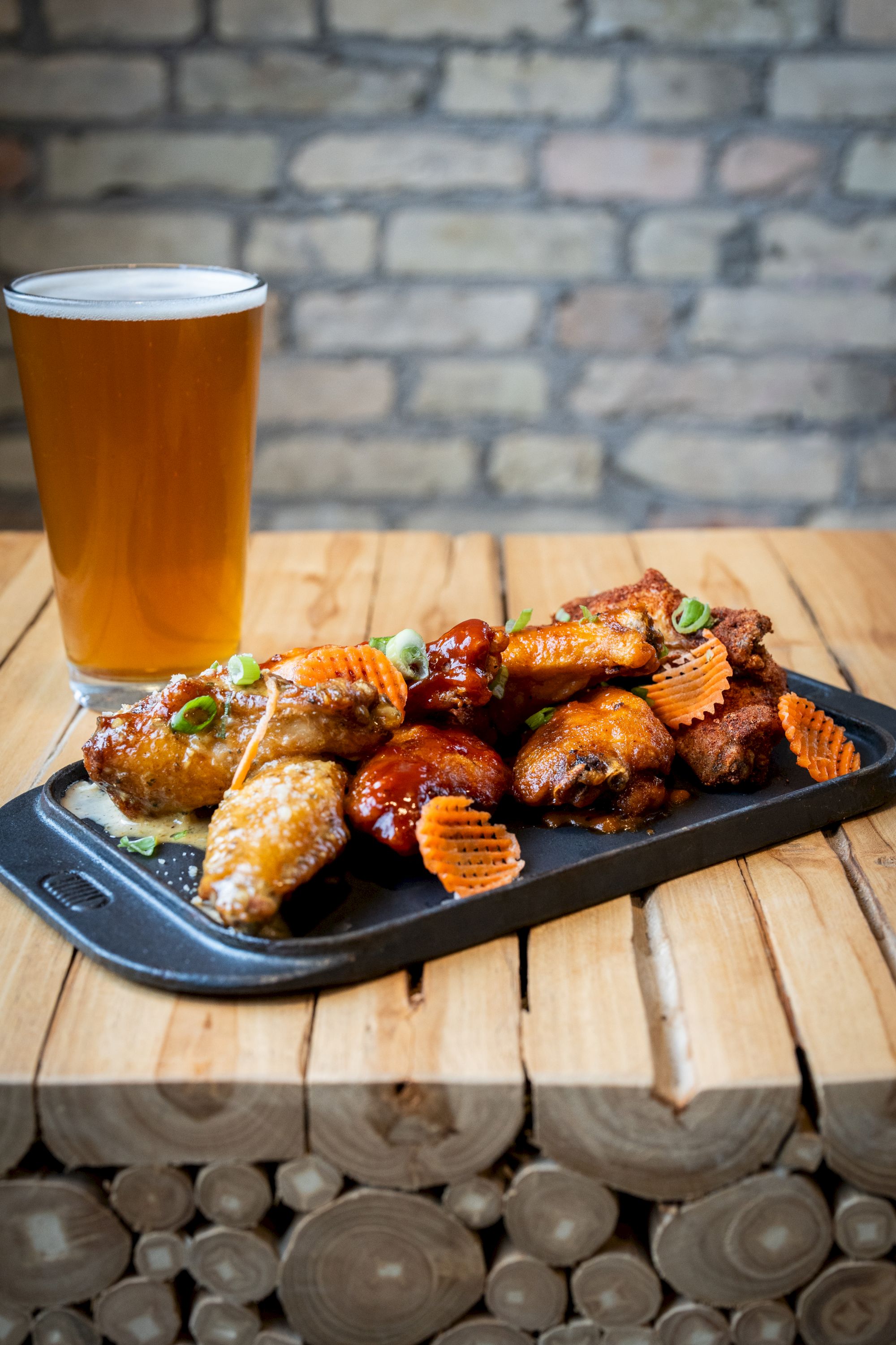 A plate of chicken wings garnished with sliced carrots and scallions is next to a pint of beer on a wooden table.