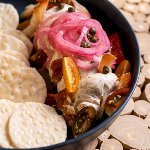 A plate with crackers, pickled onions, cream cheese, capers, and citrus slices, arranged on a wooden surface ends the sentence.