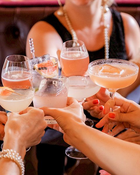 A group of people are clinking glasses filled with various cocktails and drinks, suggesting a celebratory gathering or toast.