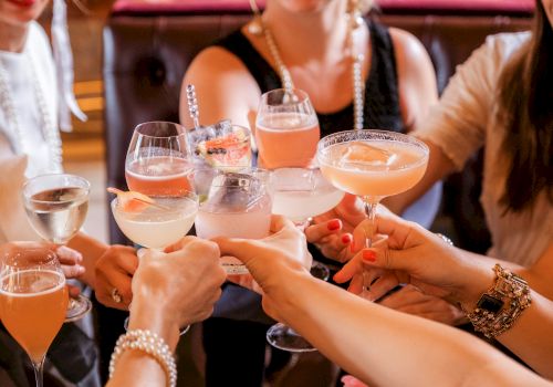 A group of people are clinking glasses filled with various cocktails and drinks, suggesting a celebratory gathering or toast.