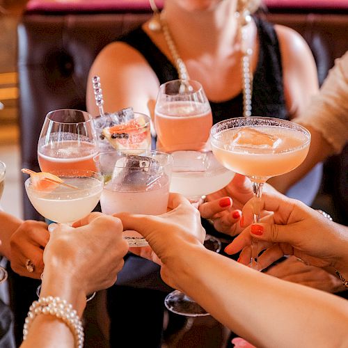 A group of people are clinking glasses filled with various cocktails and drinks, suggesting a celebratory gathering or toast.